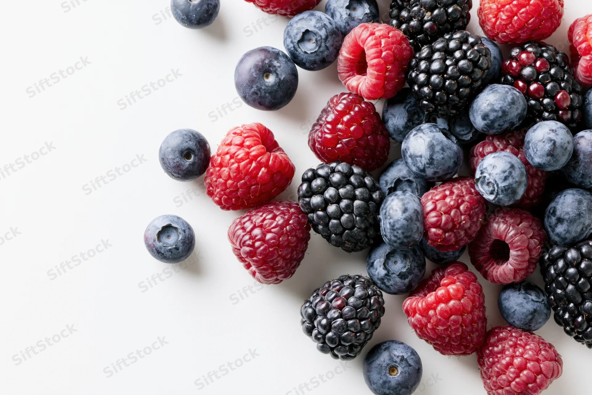 Mixed fresh blueberries raspberries and blackberries scattered on white surface