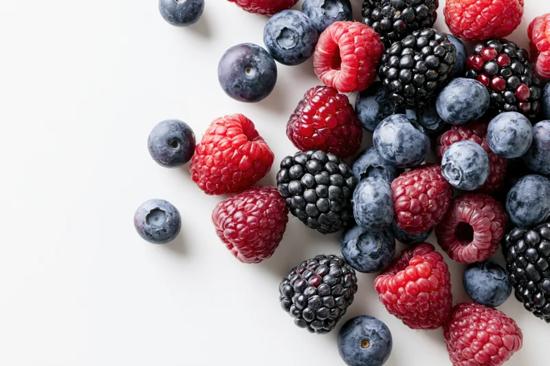 Mixed fresh blueberries raspberries and blackberries scattered on white surface