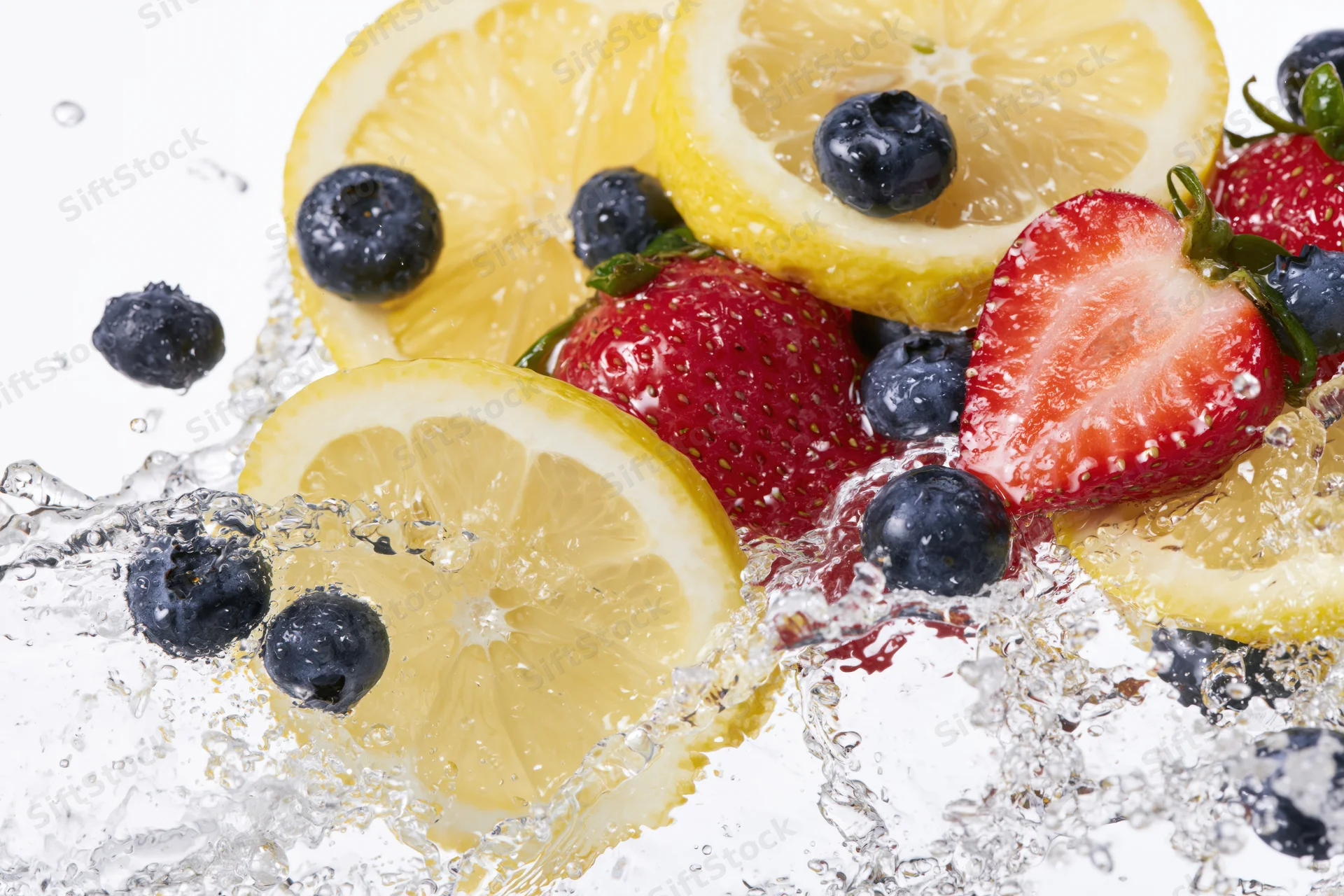 Lemon slices, strawberries and blueberries splashing in water on white background