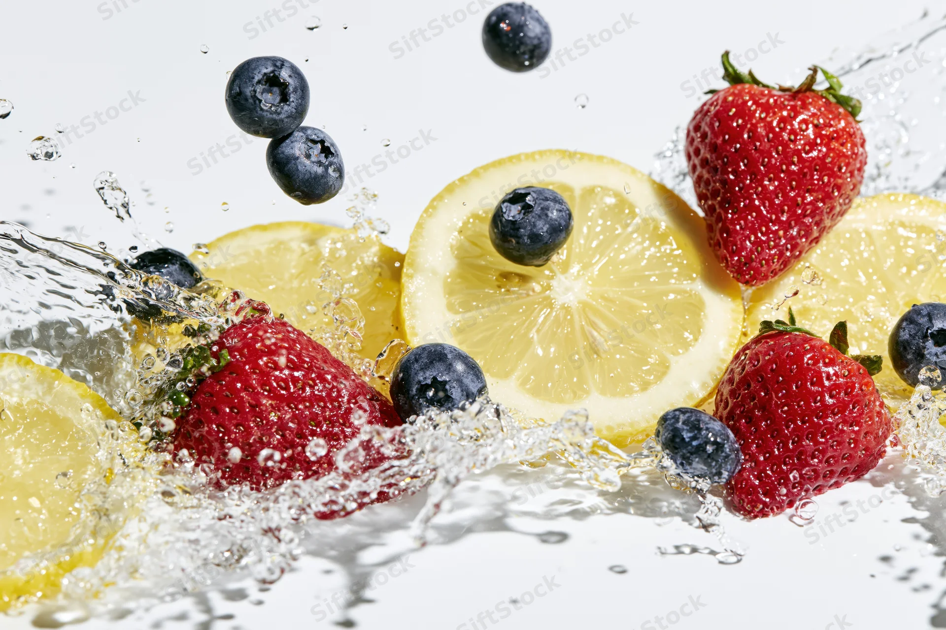Lemon slices, strawberries and blueberries splashing in water on white background