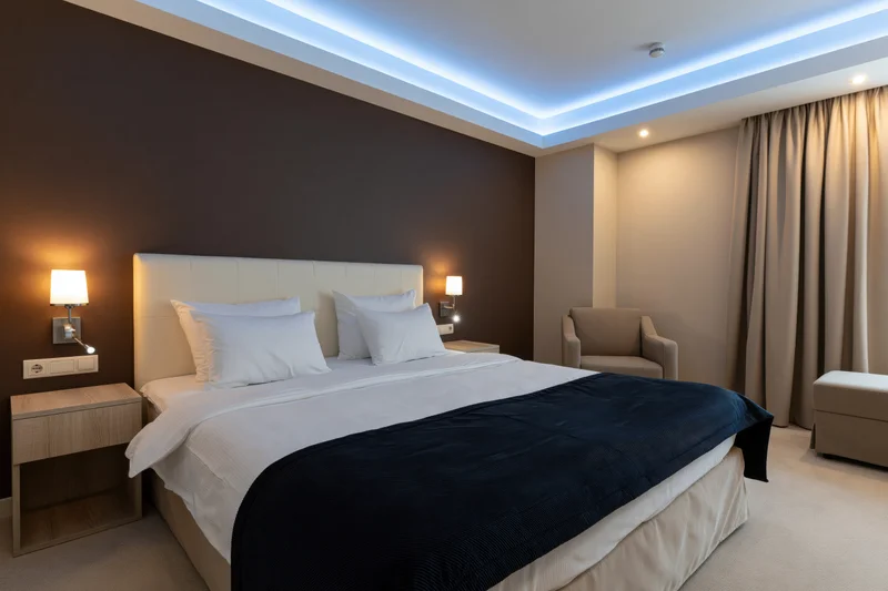 Modern hotel bedroom with double bed centered under led ceiling lighting and warm wall sconces