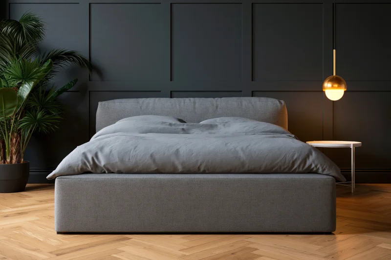 Modern minimalist bedroom with grey upholstered bed, dark paneled walls, and warm pendant light over wooden herringbone flooring