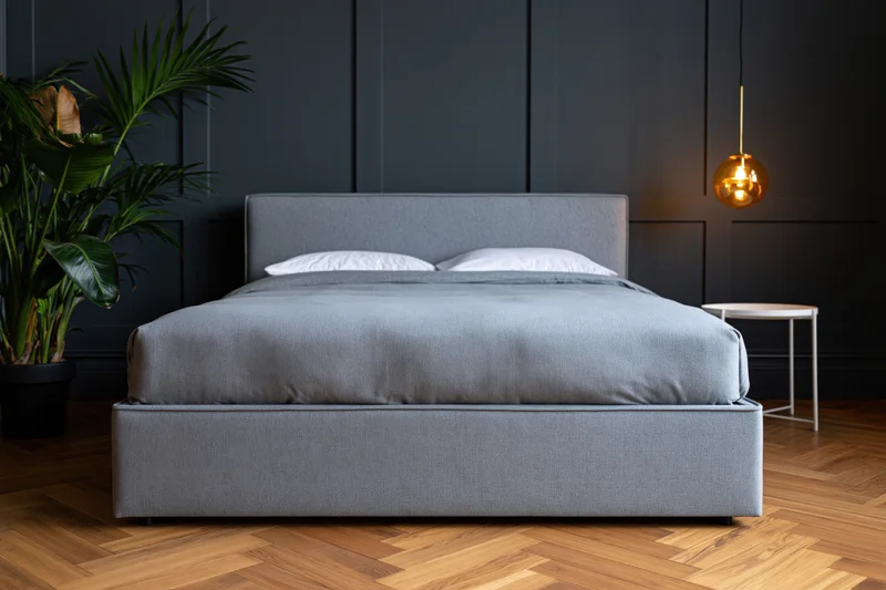 Grey upholstered bed with white pillows and gold pendant lamp in modern minimalist bedroom with dark paneled walls and wooden parquet flooring