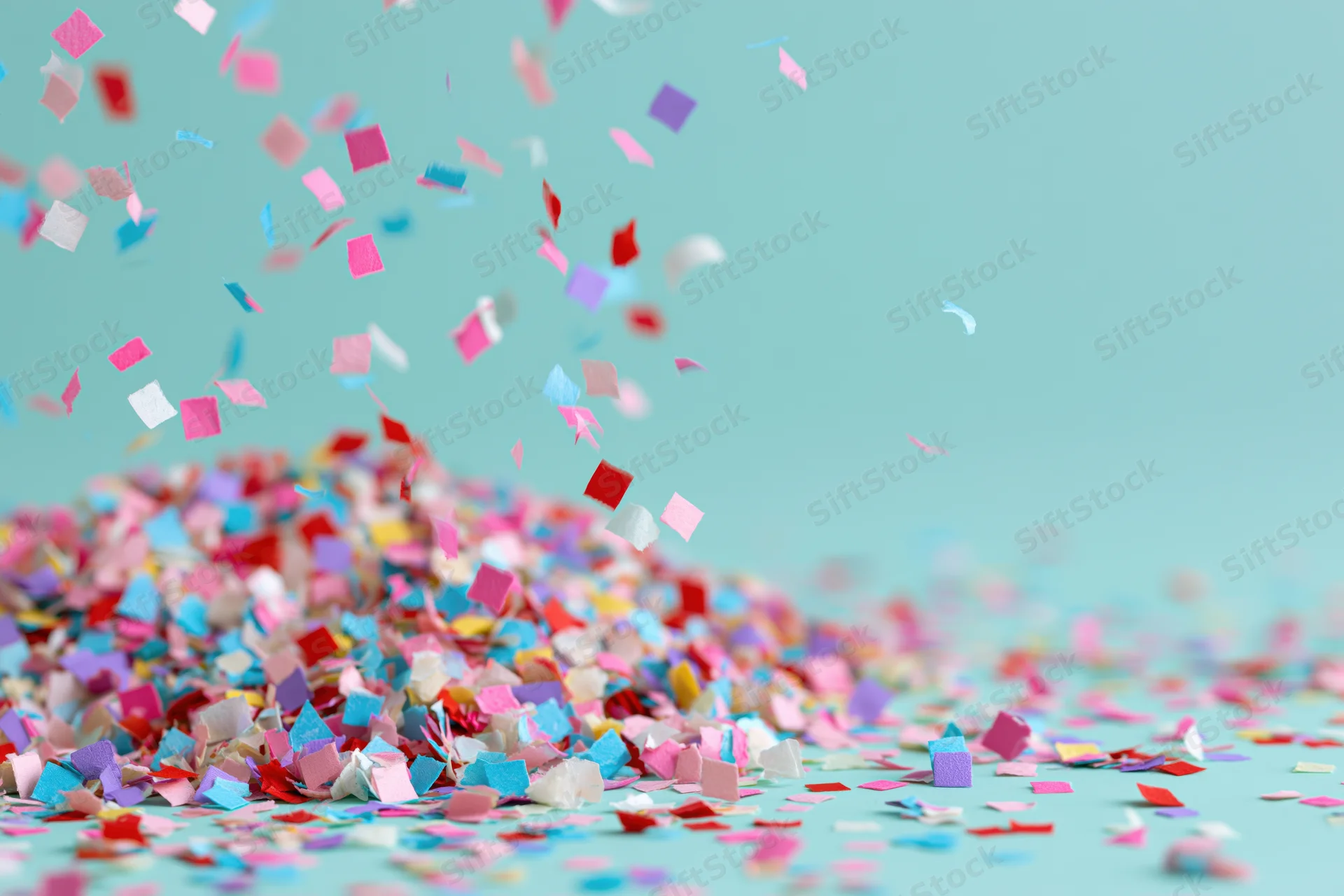 Multicolored paper confetti falling and scattered on a teal surface with copyspace on the right