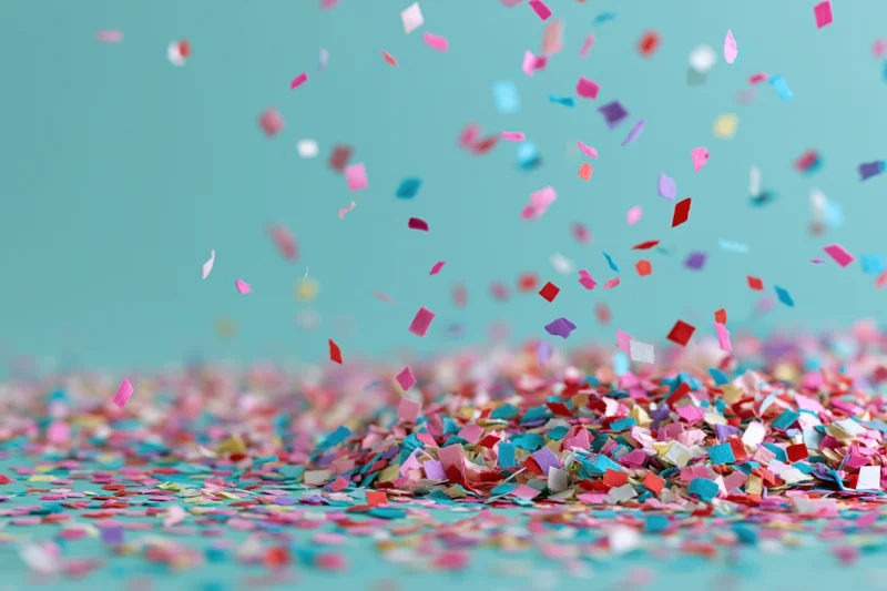 Multicolored paper confetti falling and scattered on a teal surface