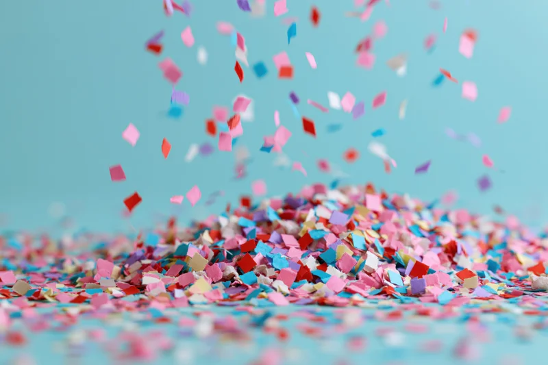 Multicolored paper confetti falling and scattered on a blue surface