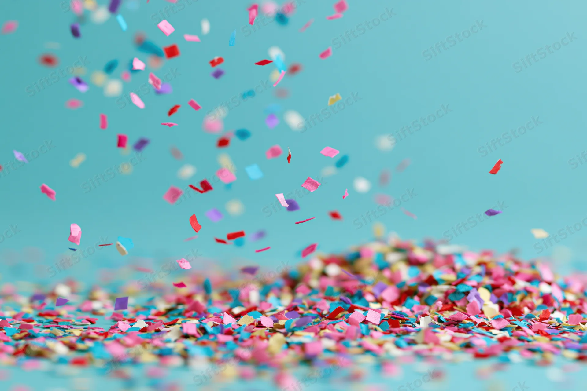 Multicolored paper confetti falling and scattered across a teal surface