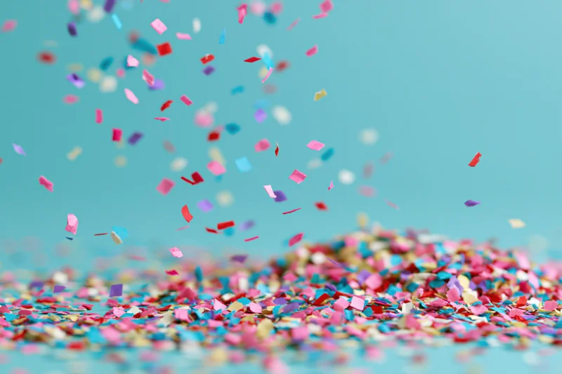 Multicolored paper confetti falling and scattered across a teal surface