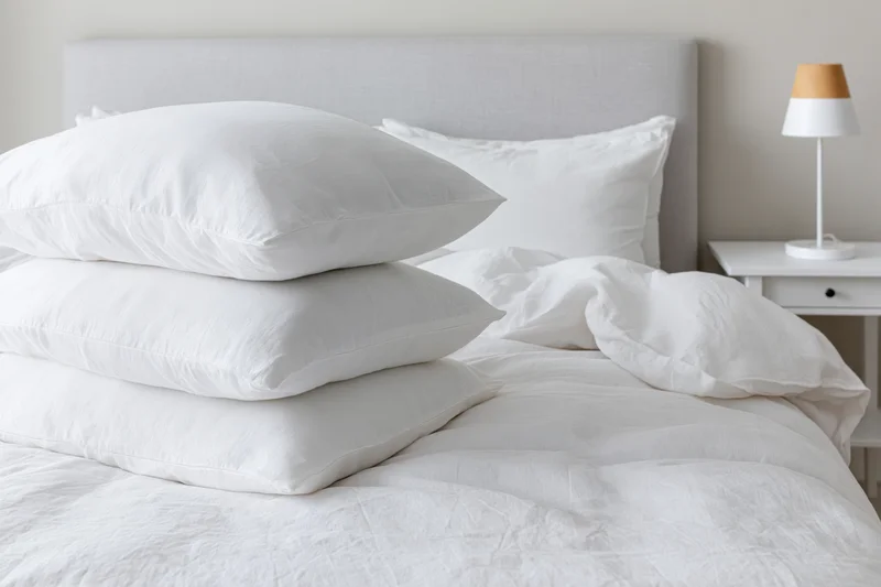 Stack of white pillows on a neatly made bed in a minimalist bedroom