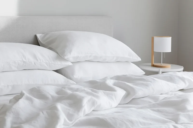White bedding with four pillows arranged against a headboard in a minimalist bedroom