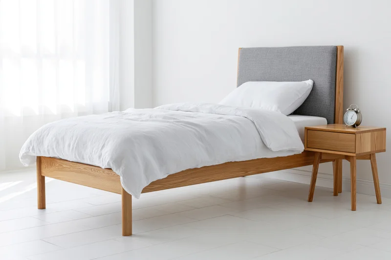 Single bed with white linen duvet and wooden frame beside a matching nightstand in a bright minimalist bedroom