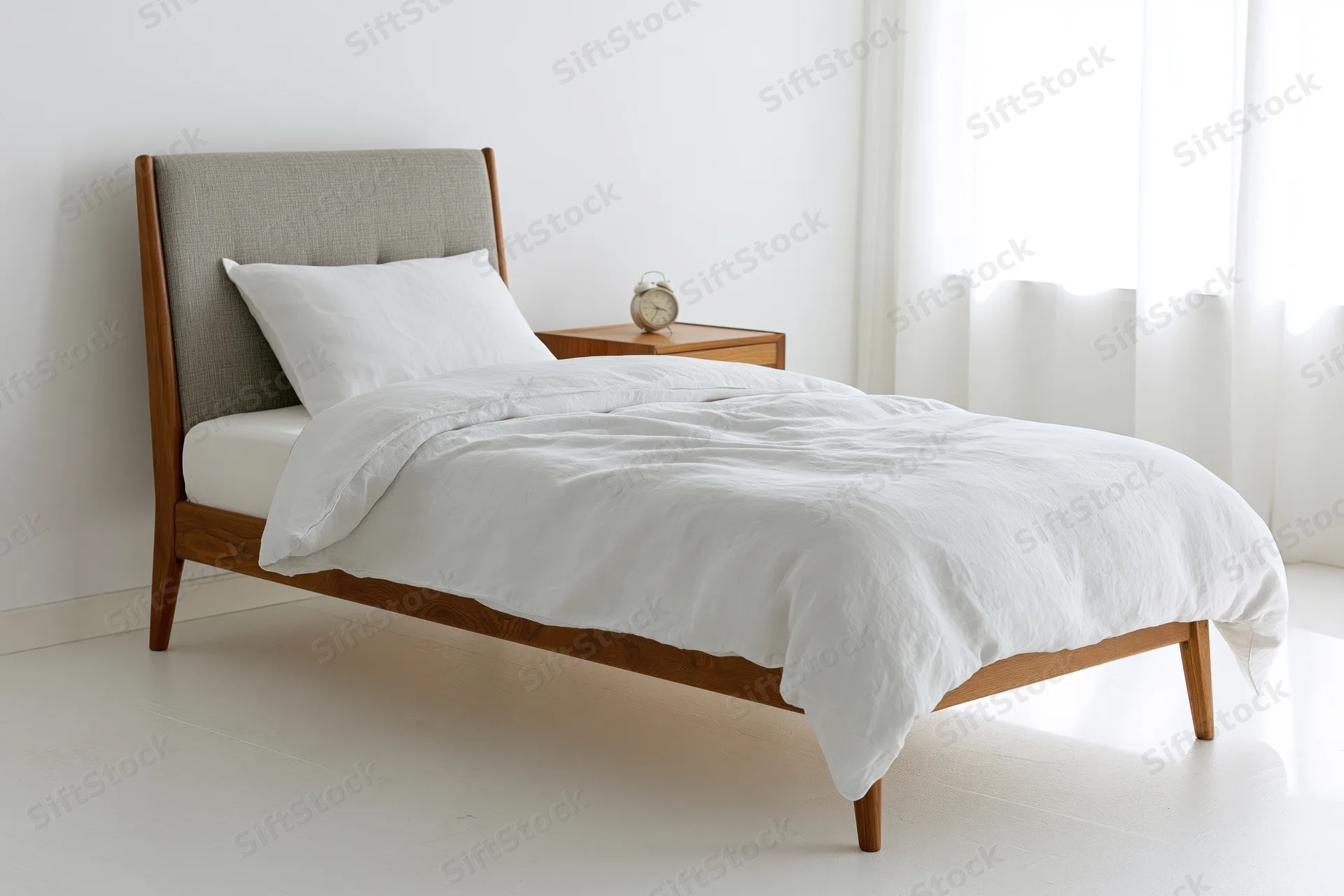 Wooden bed with white linen duvet and headboard in minimalist bedroom with nightstand and alarm clock near window
