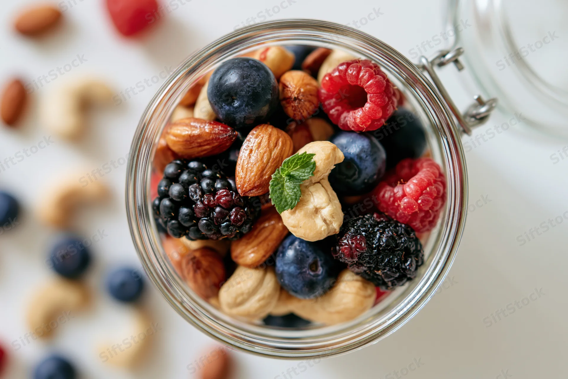 Glass jar filled with mixed nuts and berries viewed from above on white surface
