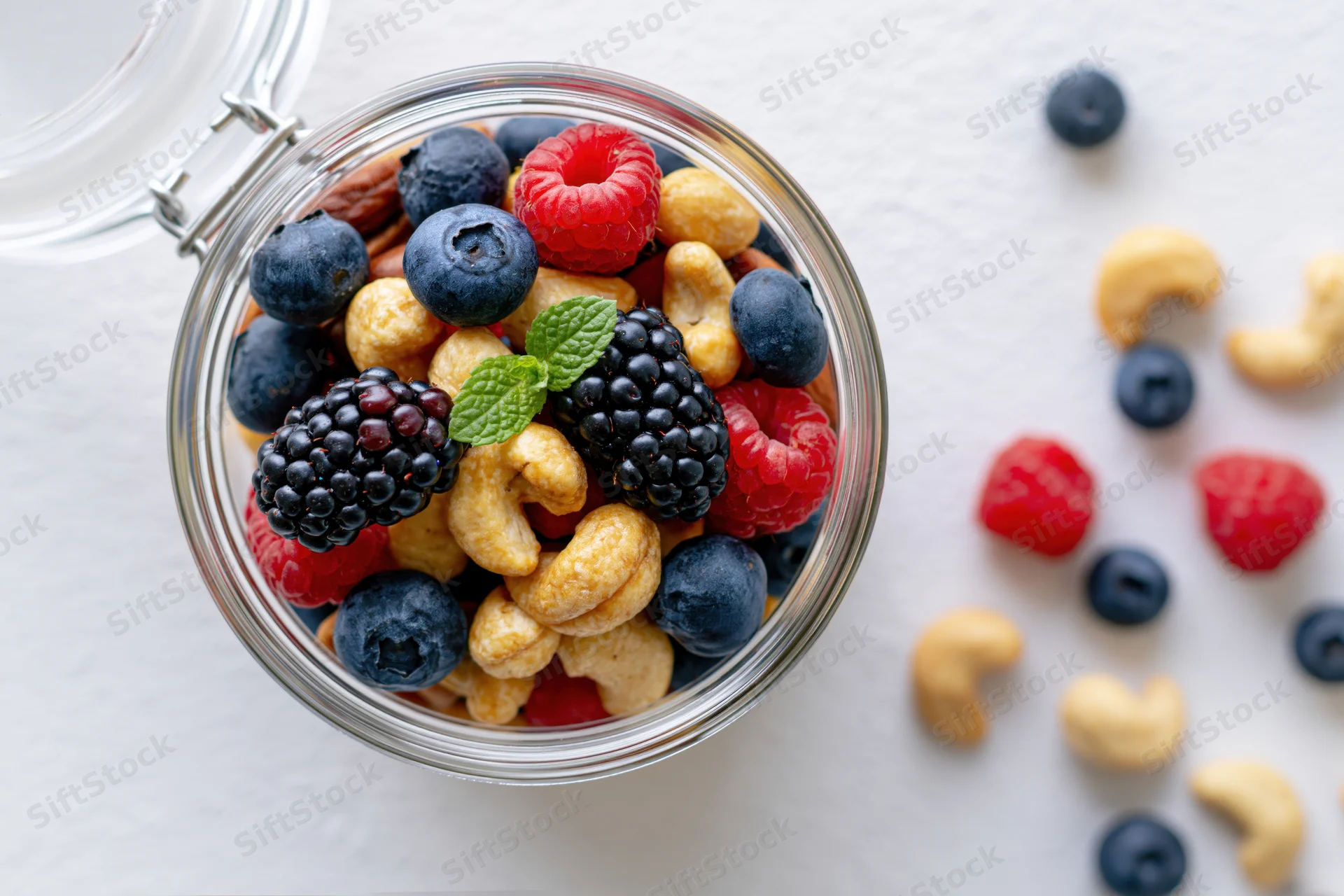 Glass jar filled with mixed nuts and berries on white surface