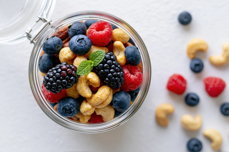 Glass jar filled with mixed nuts and berries on white surface