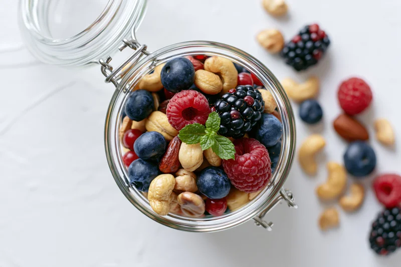 Glass jar filled with mixed nuts and berries on white marble surface