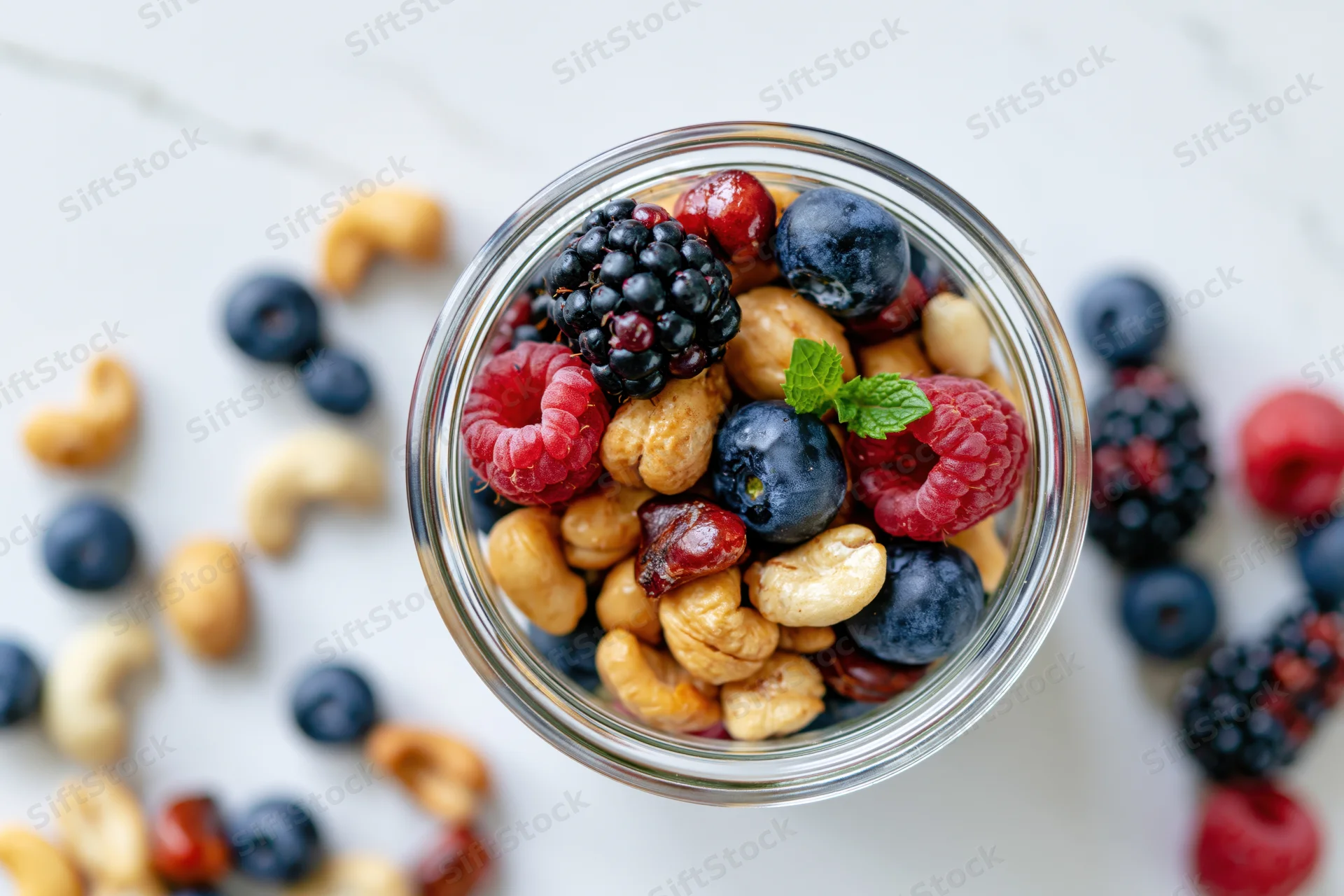 Glass jar filled with mixed nuts and berries on a marble surface