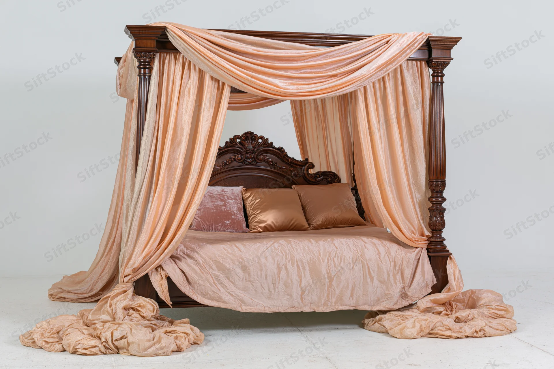 Ornate wooden four-poster canopy bed with draped peach fabric and pillows on white background