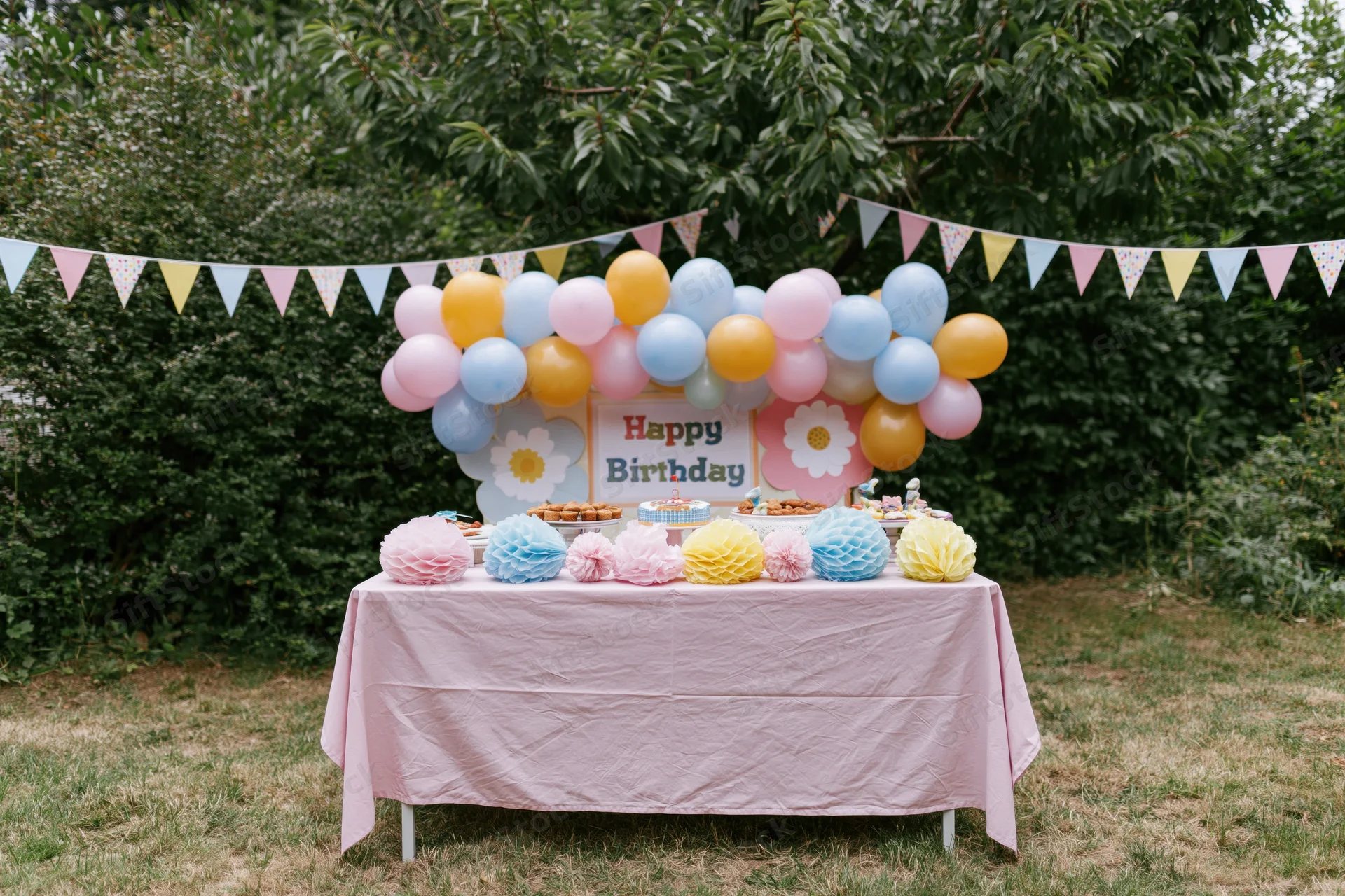 Birthday party table decorated with balloons and pastel honeycomb pompons in a backyard garden