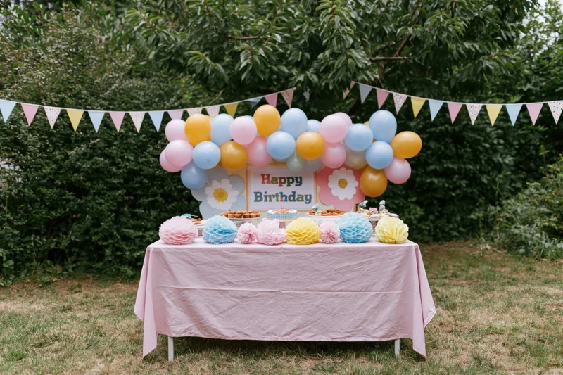 Birthday party table decorated with balloons and pastel honeycomb pompons in a backyard garden
