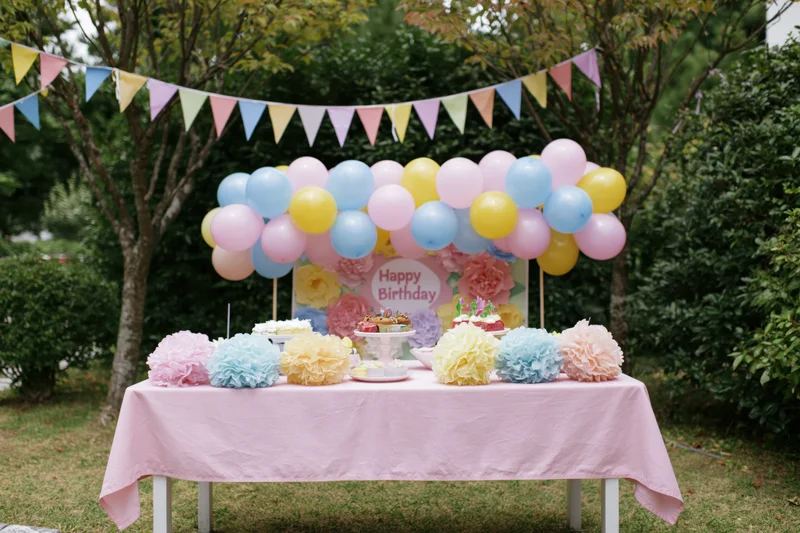 Birthday party setup with balloons and desserts on a table in a backyard garden