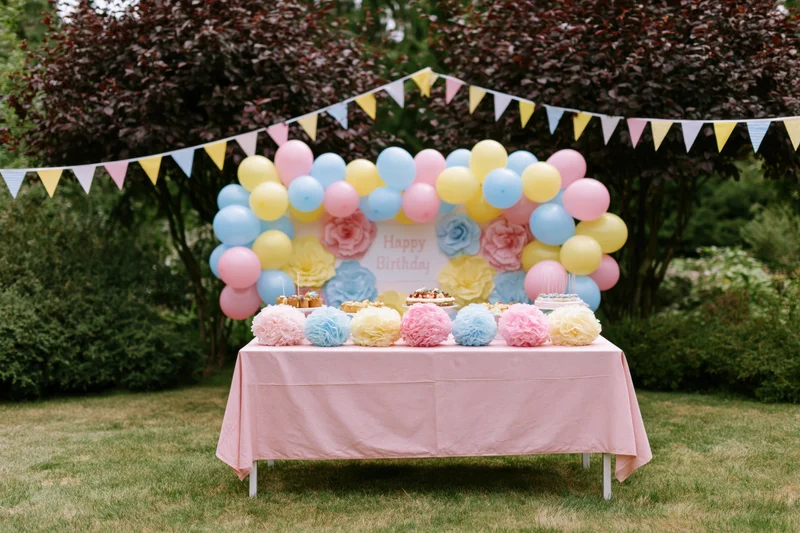 Birthday party setup with balloons and desserts on a table in a backyard garden