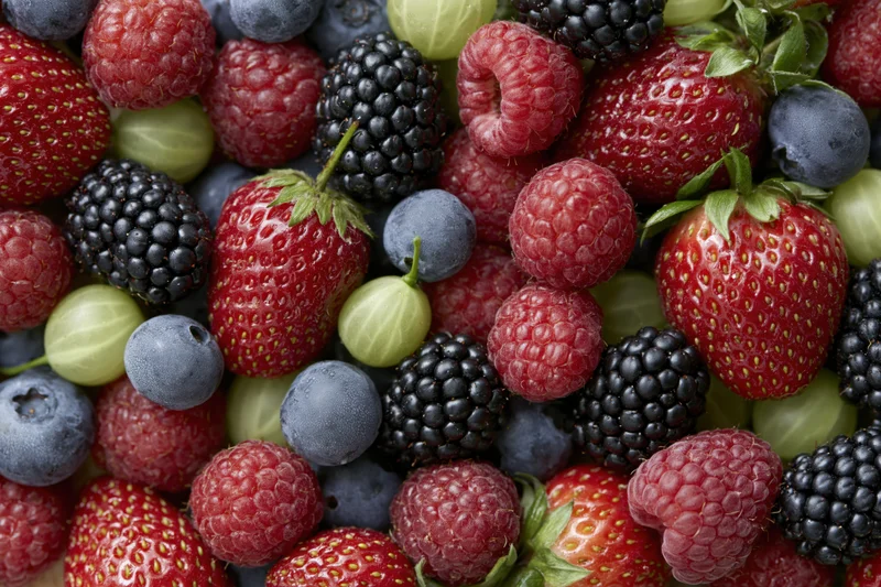 Overhead close-up of a dense pile of mixed fresh berries including strawberries, raspberries, blueberries, blackberries, and gooseberries