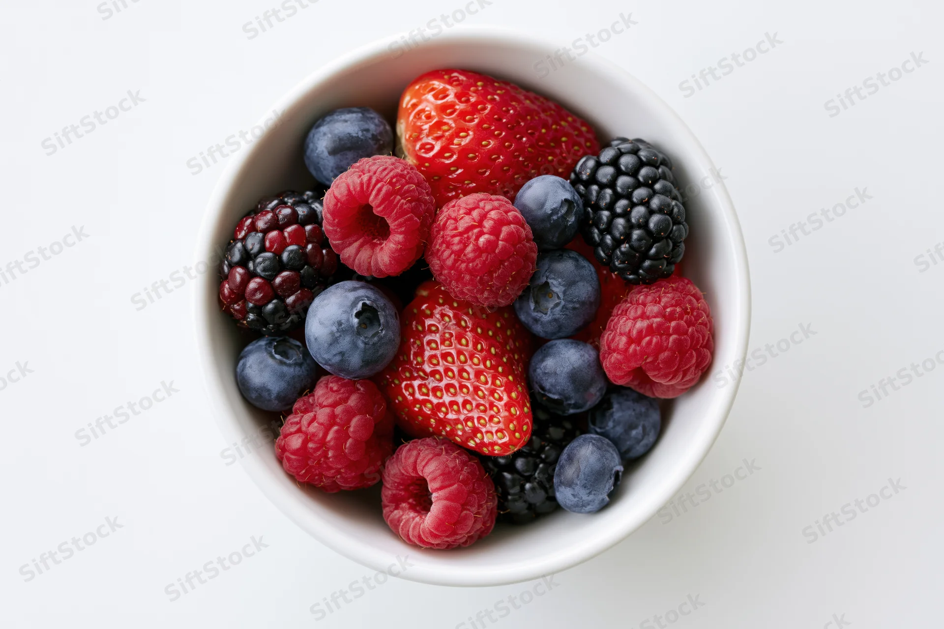 Overhead closeup of a white ceramic bowl filled with mixed berries on a white surface