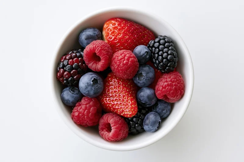 Overhead closeup of a white ceramic bowl filled with mixed berries on a white surface