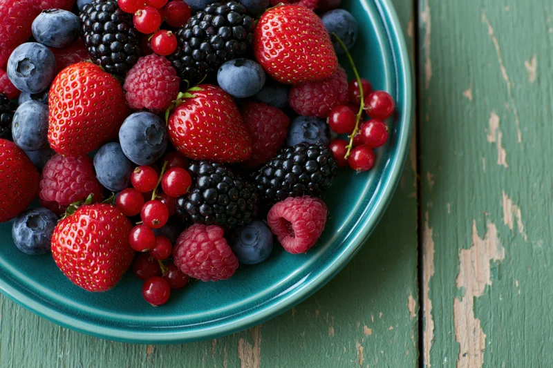 Mixed berries piled on a teal ceramic plate on a rustic wooden table