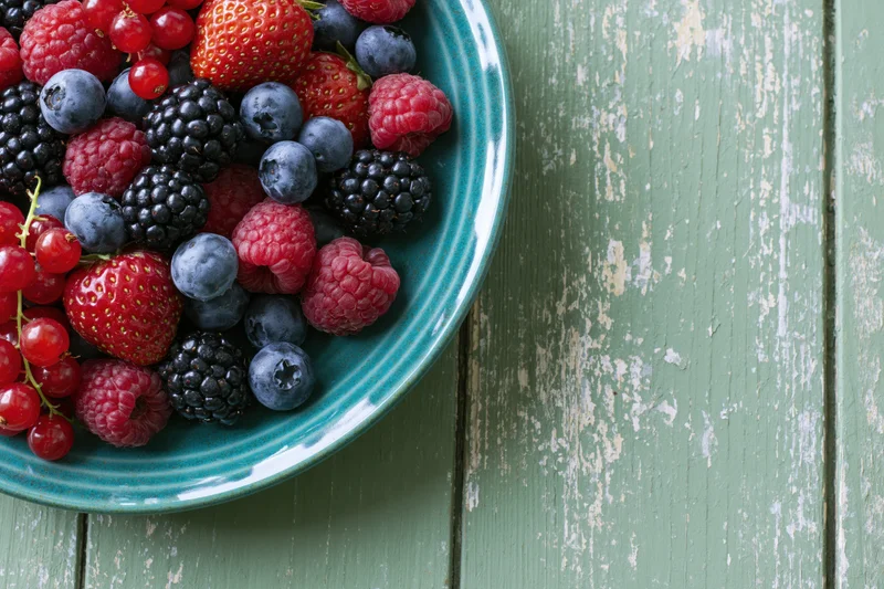 Mixed berries in a teal ceramic bowl on a weathered green wooden table