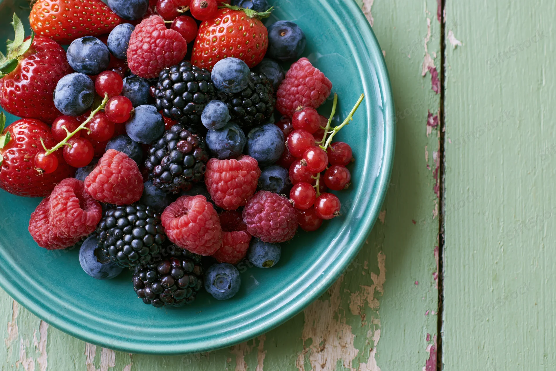 Mixed berries piled on a teal ceramic plate on a rustic wooden table