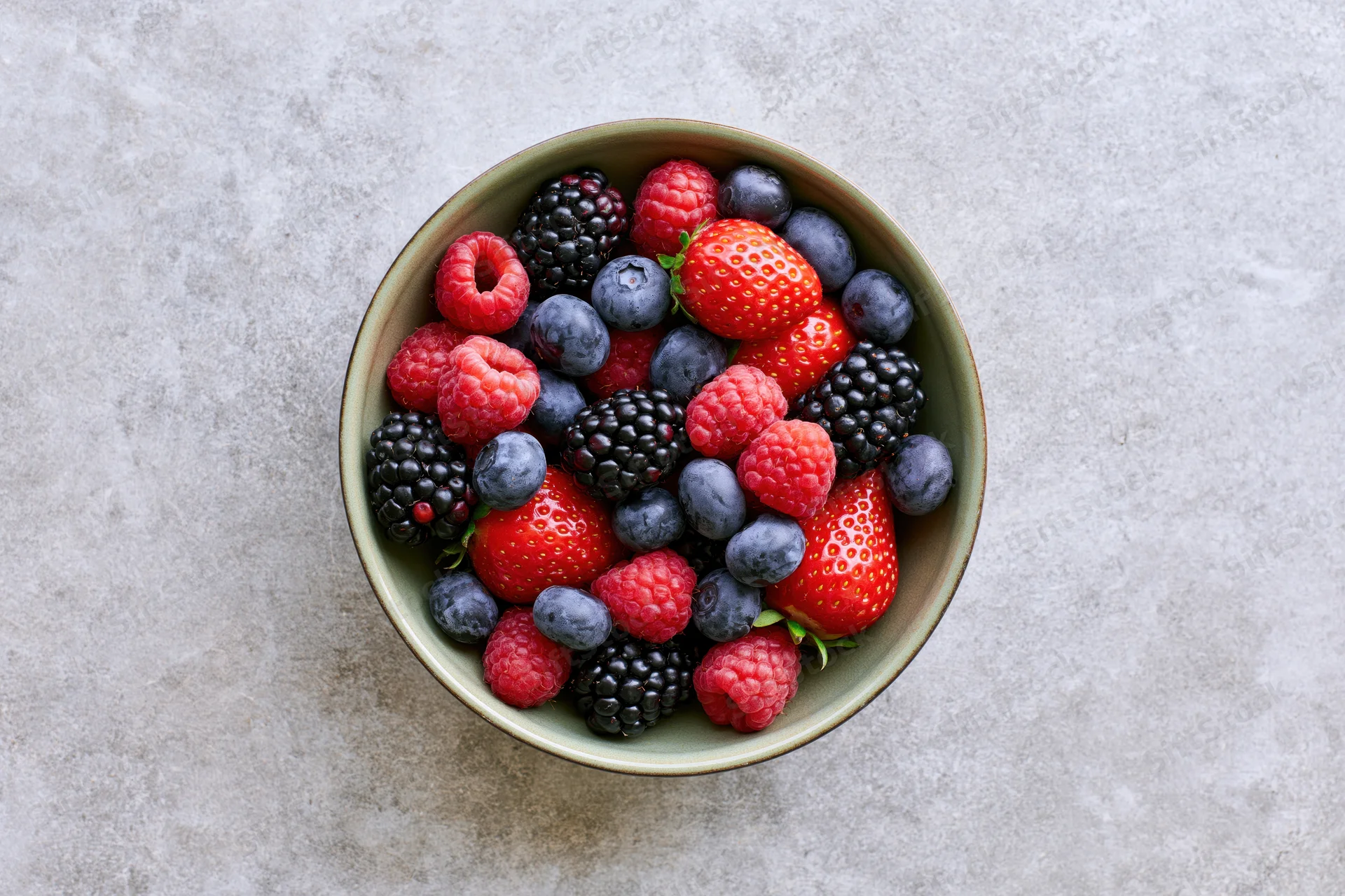Overhead view of a ceramic bowl filled with mixed fresh berries on a stone countertop