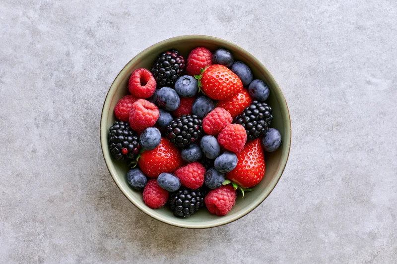 Overhead view of a ceramic bowl filled with mixed fresh berries on a stone countertop
