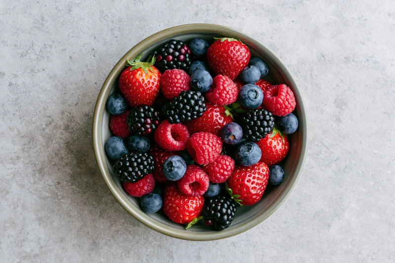 Overhead view of a ceramic bowl filled with mixed fresh berries on a gray stone surface