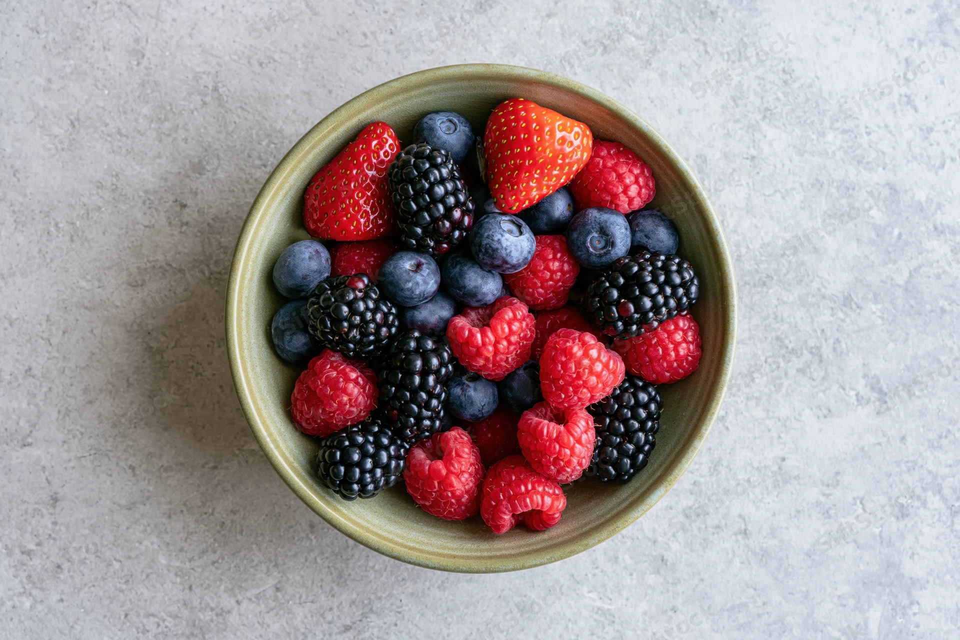 Ceramic bowl filled with mixed fresh berries on gray stone surface