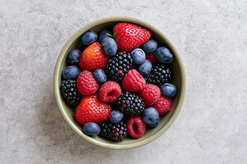 Ceramic bowl filled with mixed fresh berries on gray stone surface
