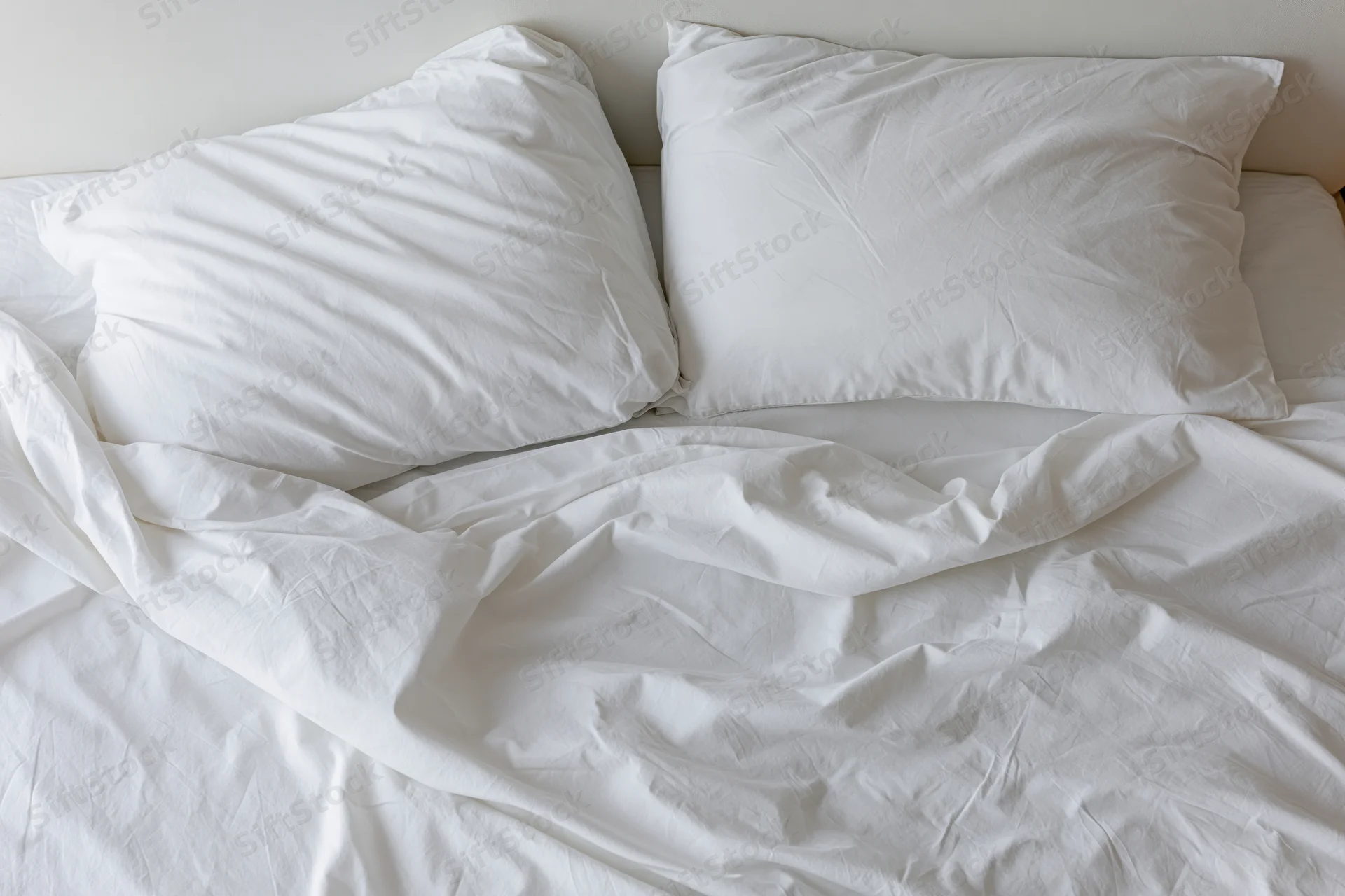 Overhead view of unmade bed with two white pillows and crumpled sheets in a bedroom