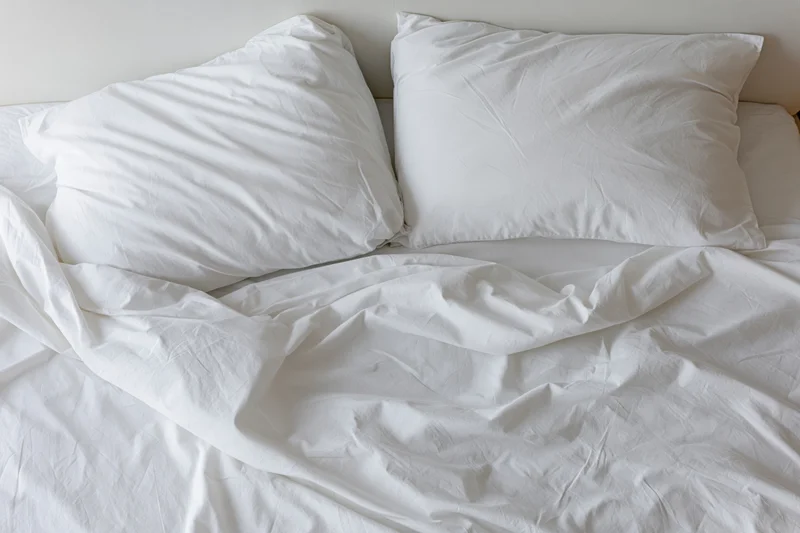 Overhead view of unmade bed with two white pillows and crumpled sheets in a bedroom