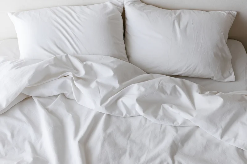 Overhead view of unmade bed with two white pillows and crumpled sheets in bedroom