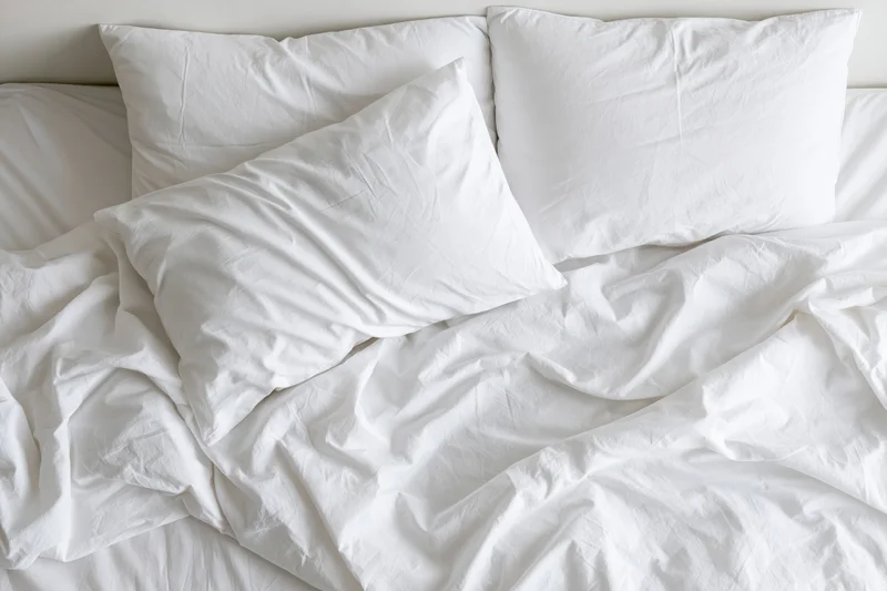Overhead view of an unmade bed with white pillows and crumpled sheets in a bedroom