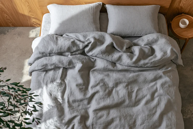Overhead view of unmade double bed with rumpled gray linen bedding and wooden headboard in a minimalist bedroom