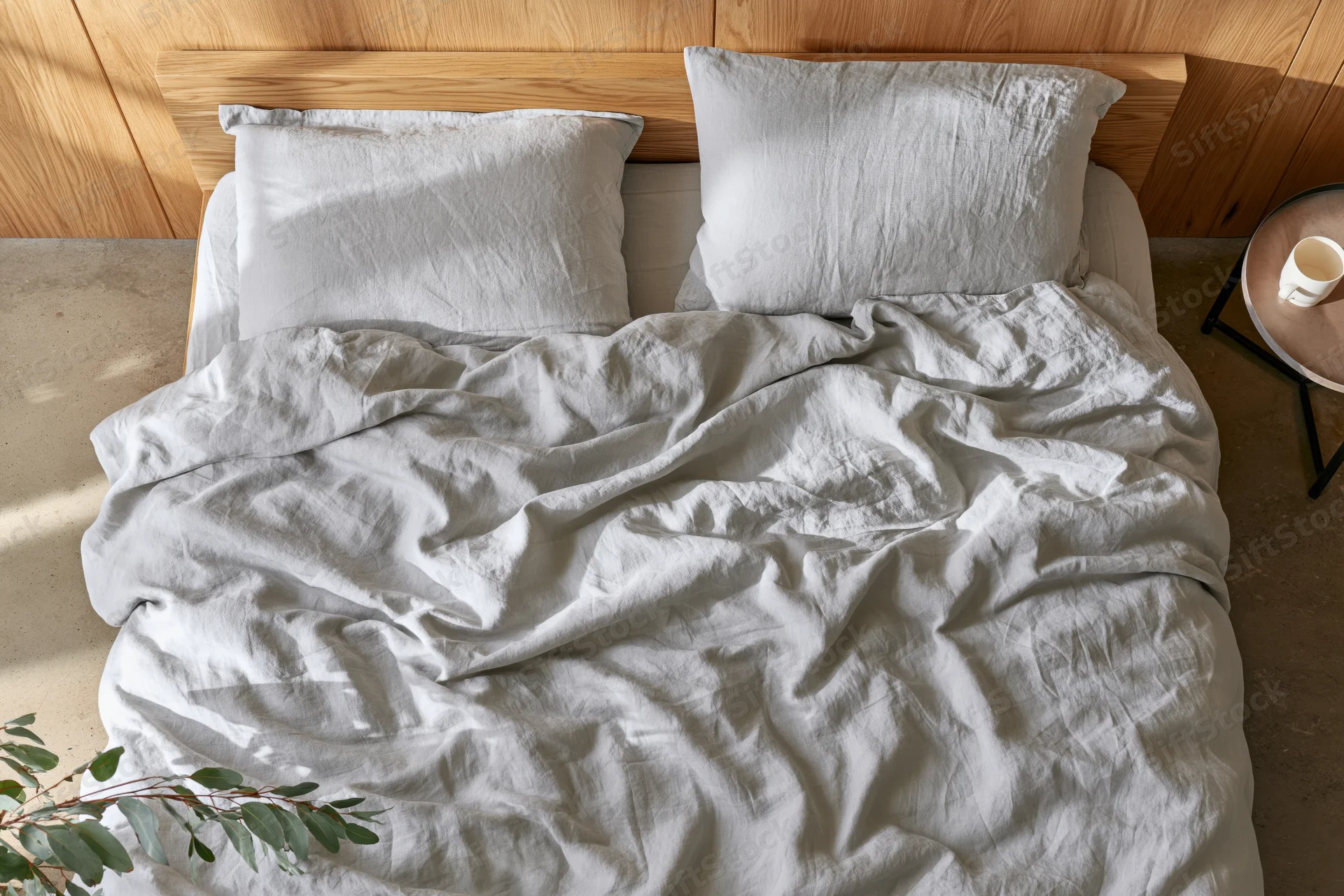 Unmade double bed with rumpled linen bedding and wooden headboard in a minimalist bedroom