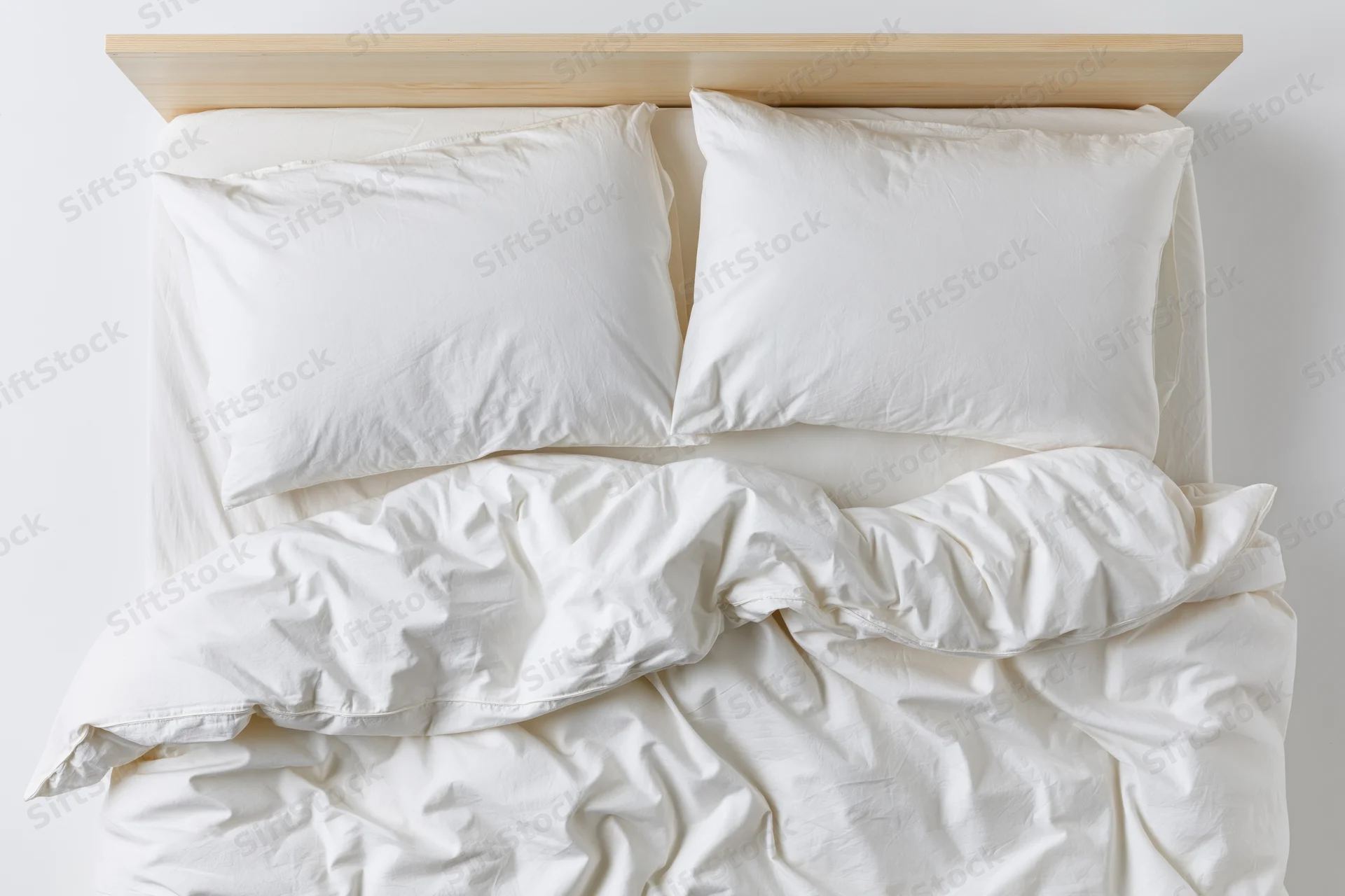 Overhead view of rumpled white bedding on a wooden headboard bed