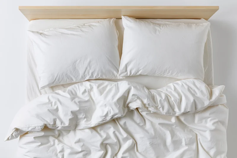 Overhead view of rumpled white bedding on a wooden headboard bed