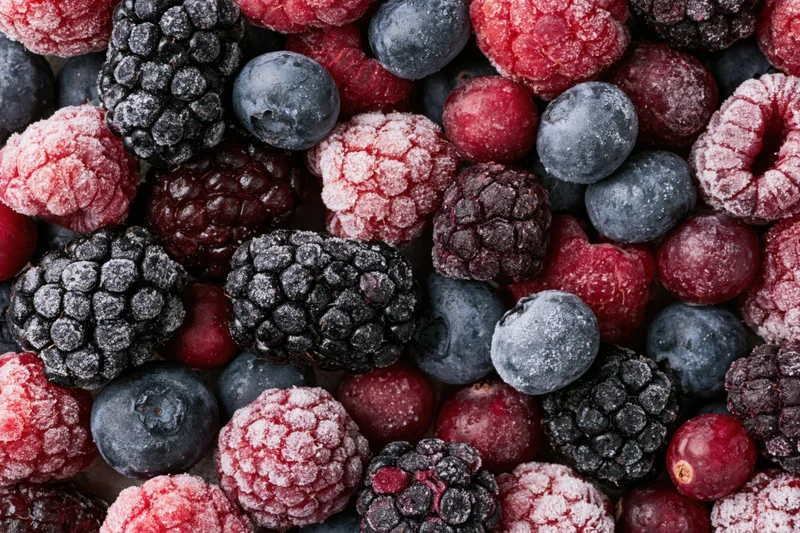 Overhead flat lay of mixed frozen berries including blackberries, blueberries, raspberries and cranberries