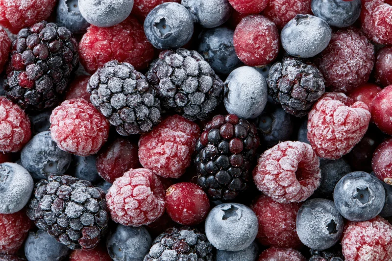 Overhead closeup of mixed frozen berries covered in frost, arranged in a flat lay