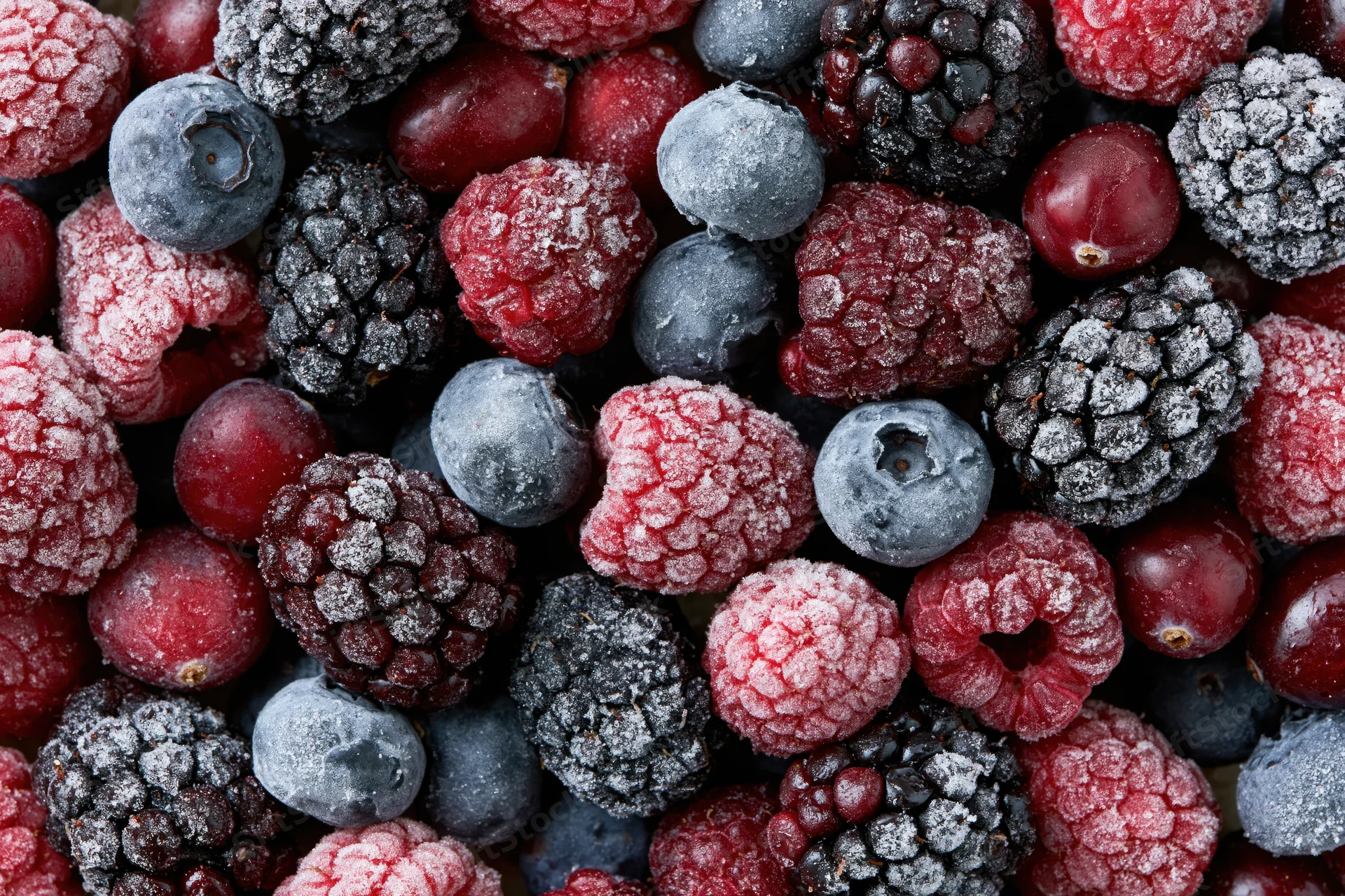 Overhead flat lay of mixed frozen berries including blueberries, blackberries, raspberries and cranberries