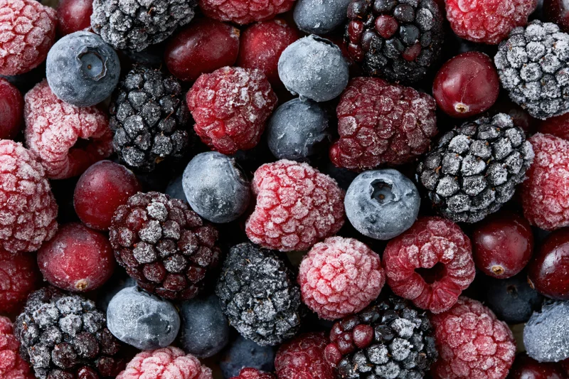 Overhead flat lay of mixed frozen berries including blueberries, blackberries, raspberries and cranberries