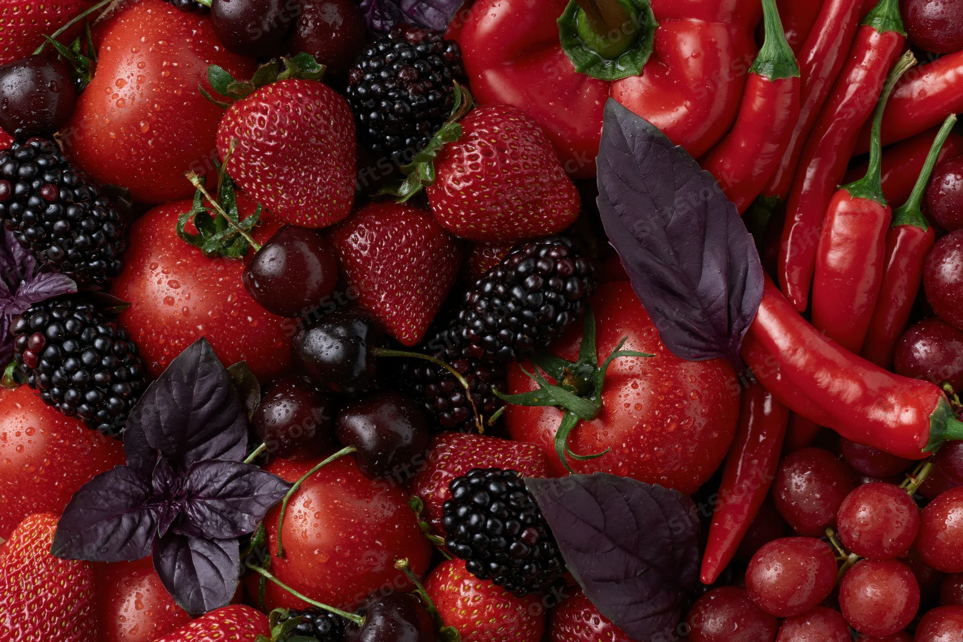 Overhead flat lay of mixed red and deep purple fruits and vegetables with basil leaves